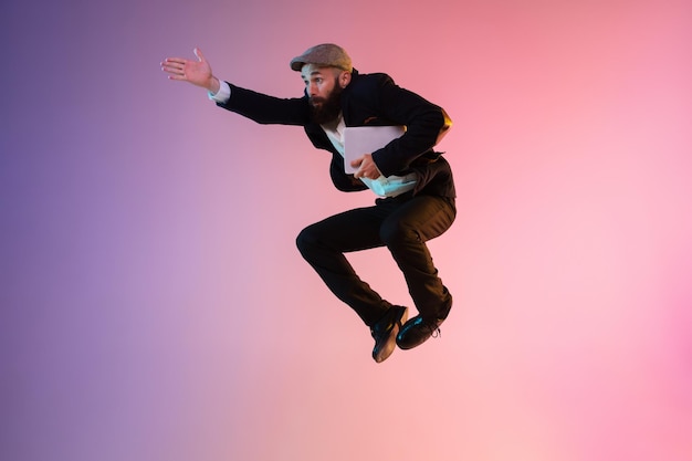 Full length portrait of happy jumping man in neon light and gradient background