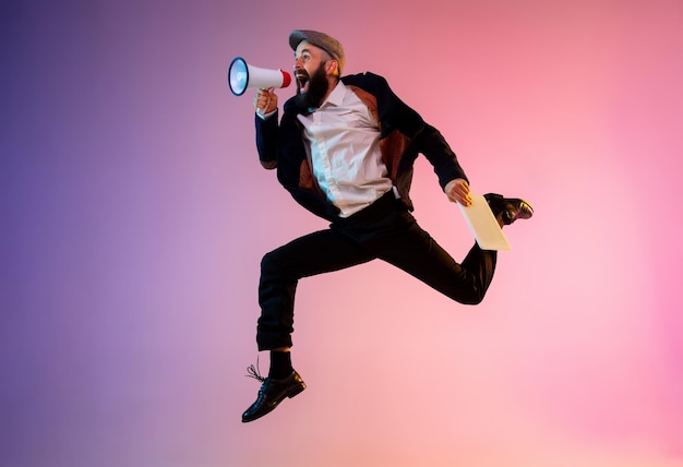 Full length portrait of happy jumping man in neon light and gradient background