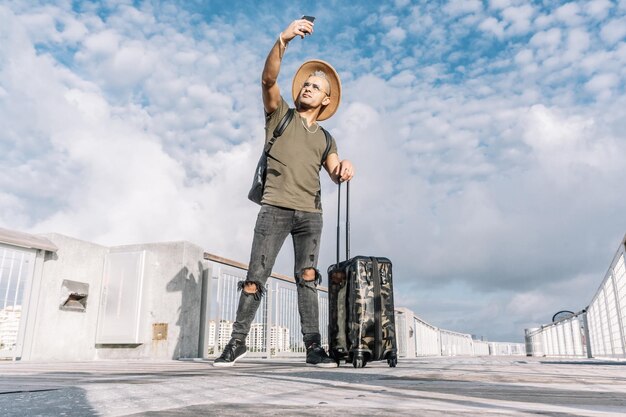 Full length portrait of a hipster man taking a selfie with a suitcase