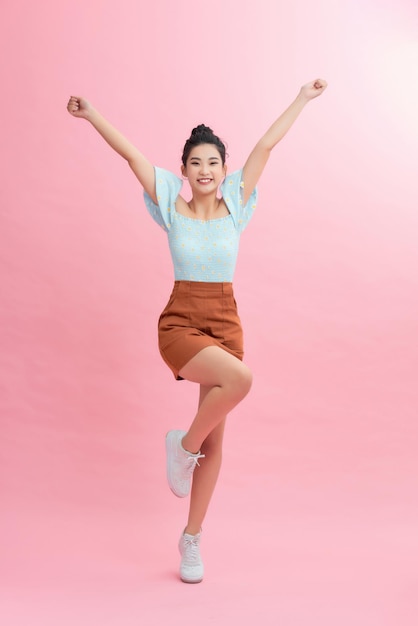 Full length portrait of a joyful young woman jumping and celebrating over pink background