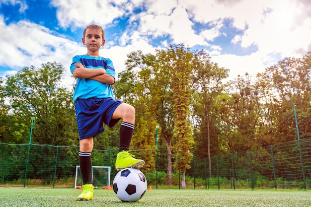 Full length portrait of a kid in sportswear posing with a soccer ball outdoors