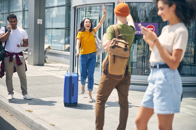 Full length portrait of laughing young lady in yellow shirt with suitcase in hand while running to the man