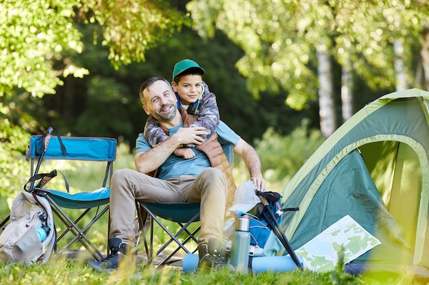 Ritratto integrale di amorevole padre e figlio e sorridere felicemente mentre si gode il viaggio in campeggio insieme nella natura, copia spazio