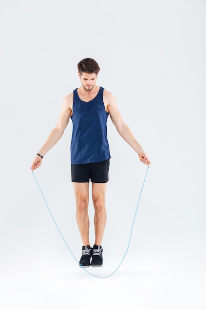 Full length portrait of a man jumping with skipping rope isolated on a gray background