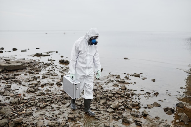 Full length portrait of man wearing hazmat suit collecting
probes by water toxic waste and pollution...