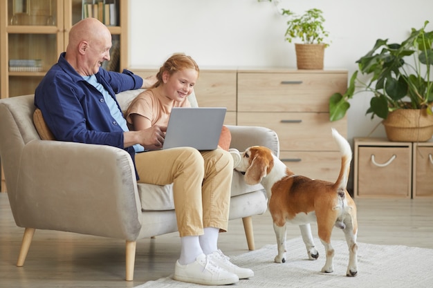 Full length portrait of modern senior man enjoying time at home with cure red haired girl and pet dog