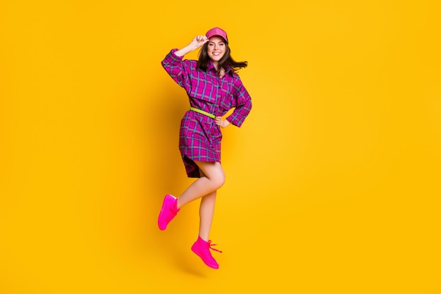 Full length portrait of nice person smile jump put hand on waist touch headwear isolated on vivid yellow color background