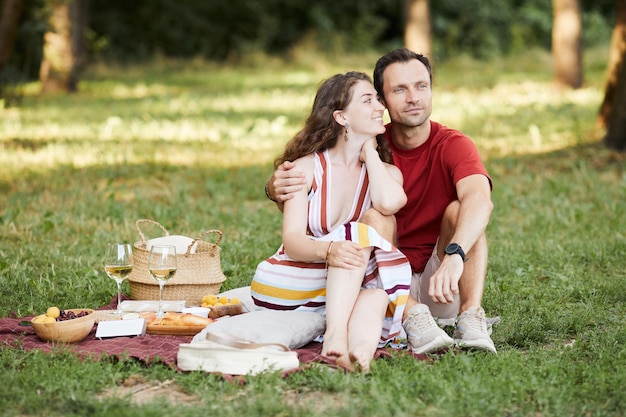 Фото Портрет счастливой молодой пары в полный рост, наслаждающейся романтическим пикником на открытом воздухе на зеленой траве