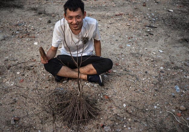 写真 畑で乾燥した植物のそばに座っている男の全身の肖像画