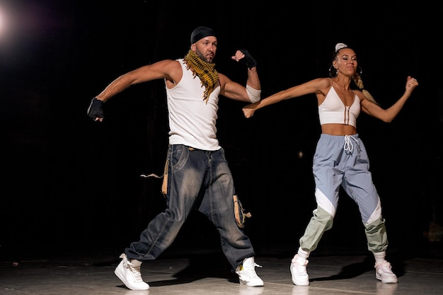 Full-length portrait ot man woman learning new hip-hop movements together in studio, wearing stylish casual outfit, energetic people full of enthusiasm, dance isolated over black background