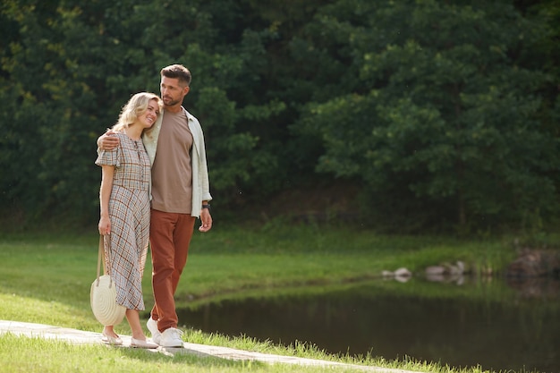 Full length Portrait of romantic adult couple embracing while walking towards lake in beautiful nature scenery