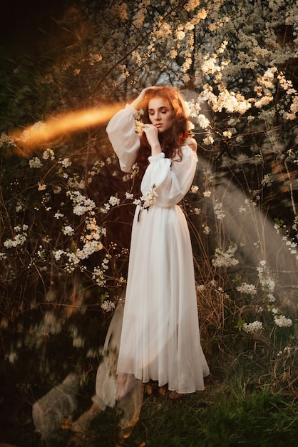 A full-length portrait of a romantic girl, looking like a forest fairy, in a blooming garden with elements of phantasmagoria. The concept of fantasy, fairy tales.