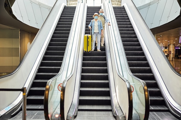 空港で移動階段を使用してフェイスマスクで年配のカップルの全身像