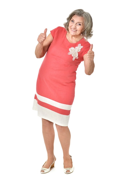 Full length portrait of senior woman in red dress with thumbs up on white background