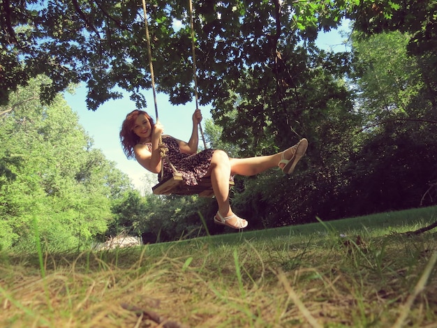 Photo full length portrait of smiling beautiful woman enjoying swing on grassy field