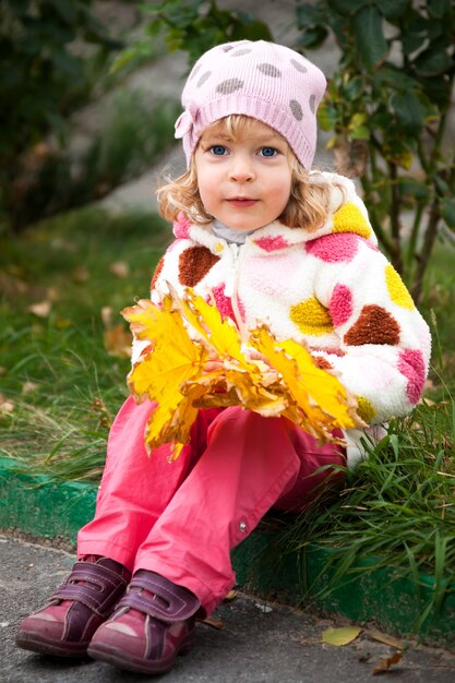 Портрет улыбающегося ребенка в полный рост с букетом желтых кленовых листьев в осеннем парке