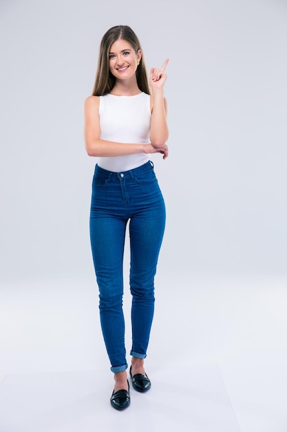 Full length portrait of a smiling female teenager pointing finger up isolated. Looking at camera