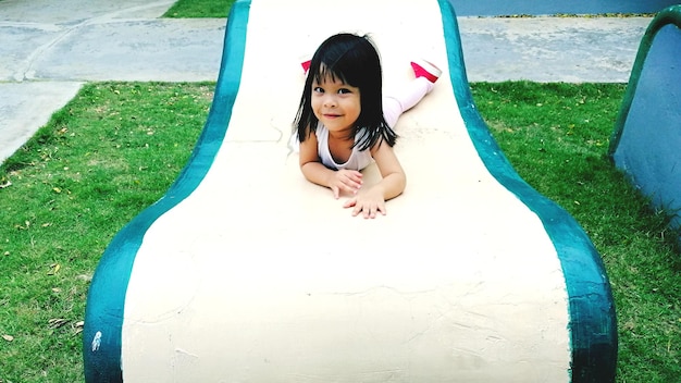 Photo full length portrait of smiling girl lying on slide at playground