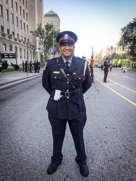 Foto ritratto a tutta lunghezza di un poliziotto sorridente in piedi sulla strada in città