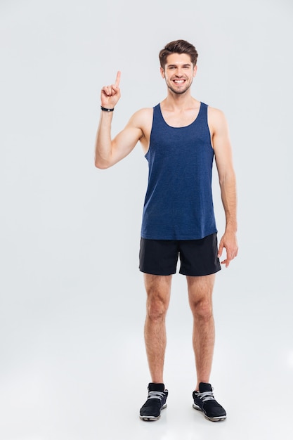 Full length portrait of a smiling sports man showing up on something over gray background