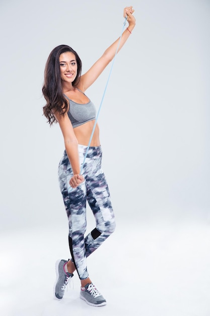 Full length portrait of a smiling sports woman holding jumping rope isolated on a white wall