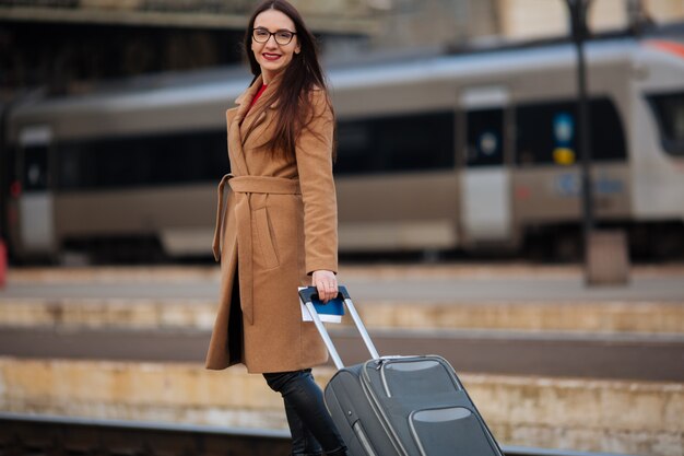 Full length portrait of smiling successful businesswoman standing at train station
