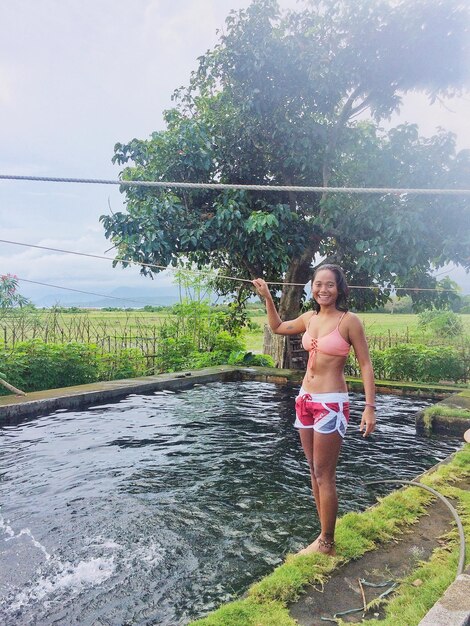 Full length portrait of smiling woman standing by pond