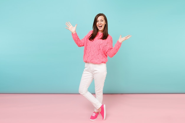 Full length portrait of smiling young woman in knitted rose sweater, white pants posing 