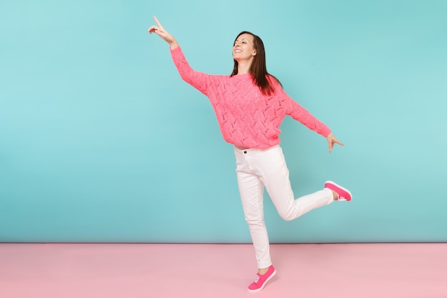 Full length portrait of smiling young woman in knitted rose sweater, white pants posing 