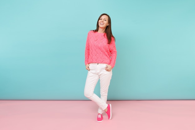 Full length portrait of smiling young woman in knitted rose sweater, white pants posing 