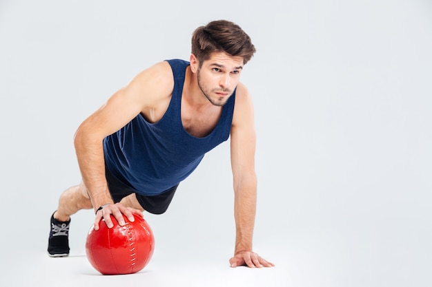 Full length portrait of a sports man workout with fitness ball isolated on a gray background