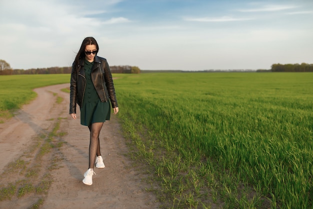 Ritratto integrale di una donna alla moda che cammina lungo un campo verde. la giovane donna sorridente sta camminando in natura. prato verde primavera