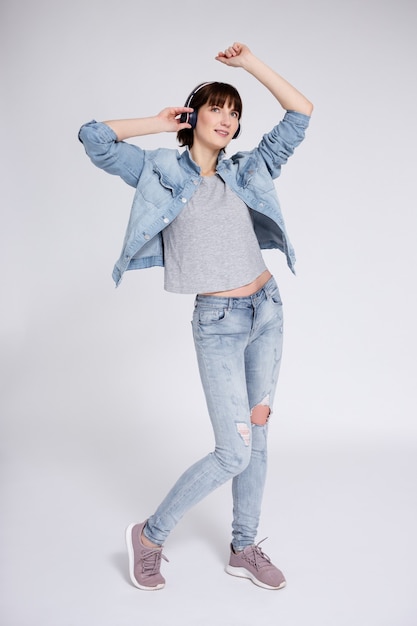 Full length portrait of teenage girl with braces on teeth listening music in headphones and dancing or celebrating something over gray background