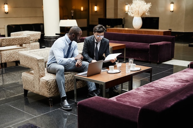 Photo full length portrait of two business people discussing work during meeting at luxurious hotel lobby, copy space