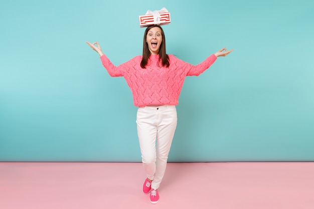 Full length portrait of woman in knitted rose sweater, white pants posing holding gift box