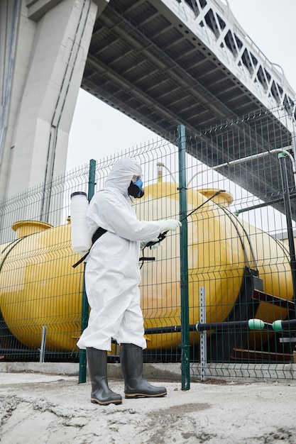 Full length portrait of worker wearing protective suit
disinfecting industrial area