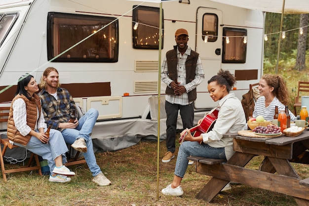 Full length portrait of young africanamerican woman playing guitar while enjoying camping outdoors w...