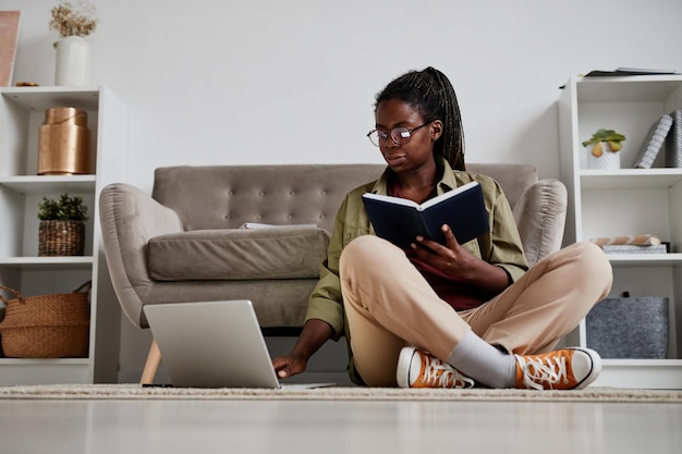 Full length portrait of young africanamerican woman working from home while sitting on floor in comf...