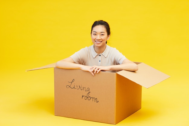 Full length portrait of young Asian woman sitting in box and smiling