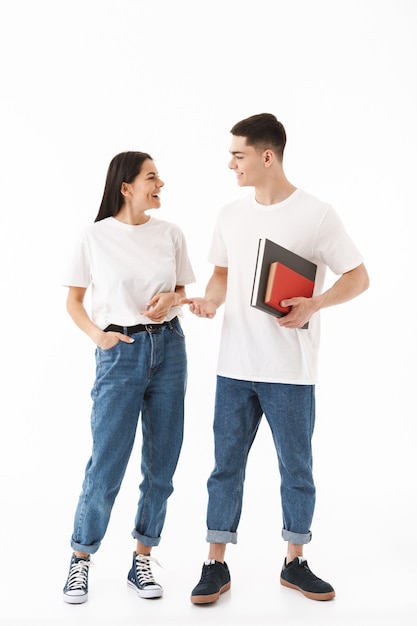 Full length portrait of a young attractive couple standing isolated over white wall, holding books