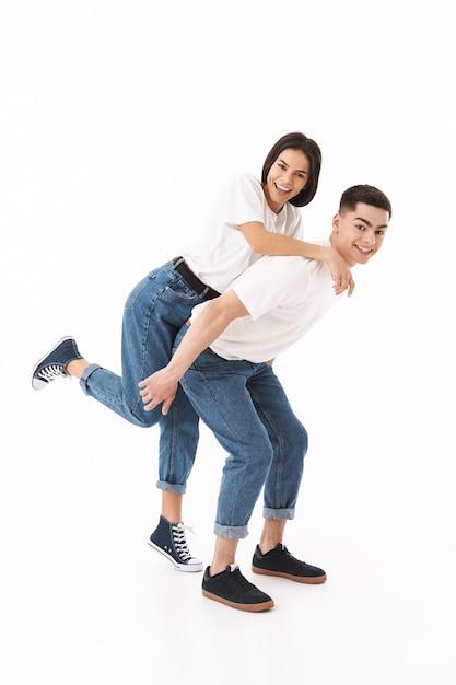 Full length portrait of a young attractive couple standing isolated over white wall, piggyback ride