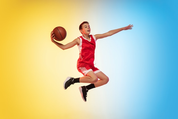 Full length portrait of a young basketball player with ball on gradient wall