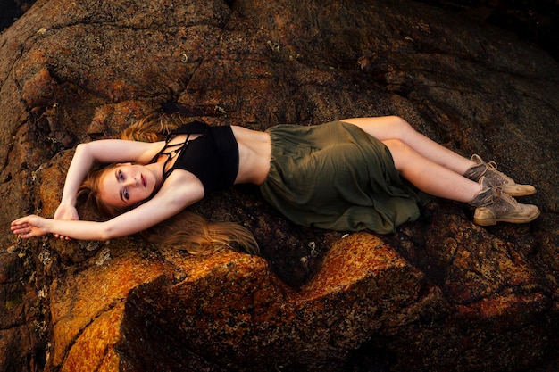 Full-length portrait young and beautiful long-haired woman in a stylish skirt and top posing on the rocks beach .feathers dreadlocks in hair and makeup boho brown style dress fashion shoes boots