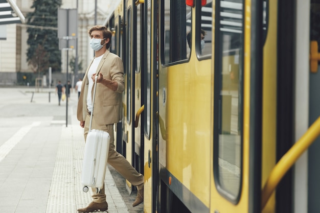 路面電車を降りる白いスーツケースとフォーマルな服装の若いビジネスマンの全身像