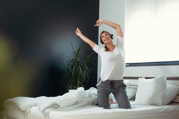 Photo full length portrait of a young casual woman in earphones listening to music in pajamas