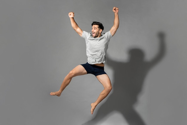Full length portrait of young fresh energetic man wearing\
sleepwear jumping in mid-air after wake up from a good sleep in the\
morning