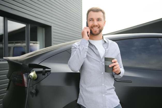 Full length portrait of young handsome bearded man in casual wear standing at the charging station