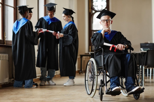 Full length portrait of young man with disability at graduation ceremony in university copy space