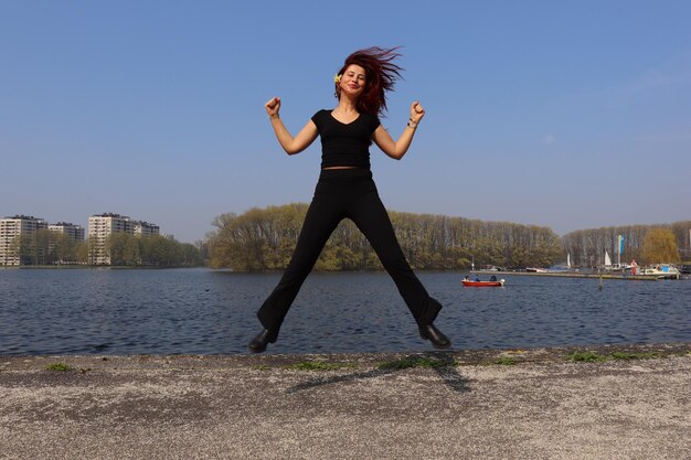 Full length portrait of young woman jumping against lake