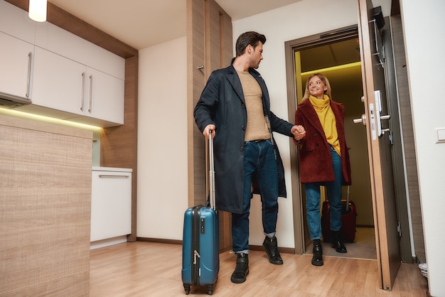 Full-length portret van jonge man en vrouw in vrijetijdskleding met koffers die hun kamer in een hotel binnenkomen. Samen reizen concept. Horizontaal schot